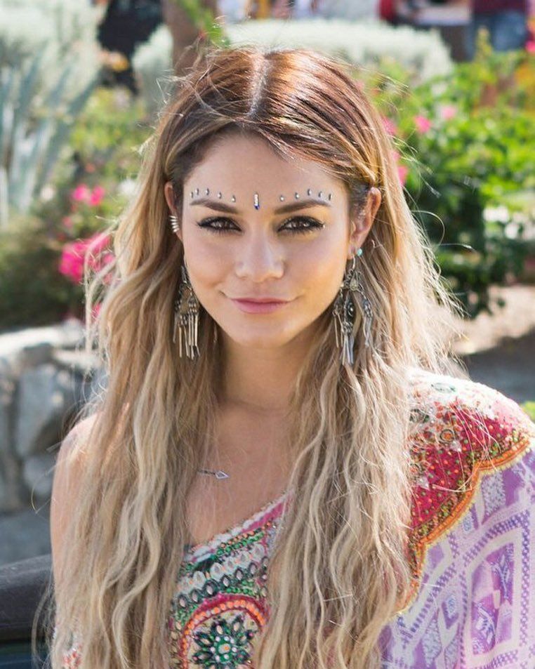 Woman wearing Indian oxidized jewelry, decorative face gems resembling a bindi arrangement, and a colorful embroidered outfit, styled in a way that evokes South Asian aesthetics—raising questions of cultural appropriation in a festival or fashion context.