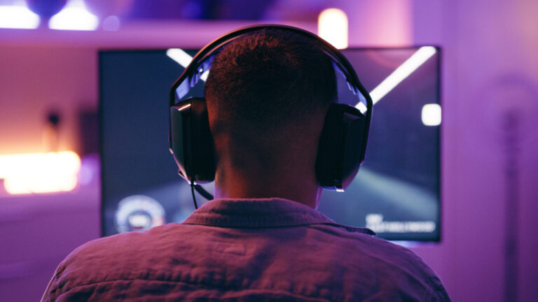 Neon, gaming and back of man with pc for live streaming esports, video games and virtual competition. Desk, computer and male gamer with headphones for playing cyber, rpg and online game on screen